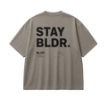 Beige t-shirt with 'STAY BLDR.' text on the back against a gray background