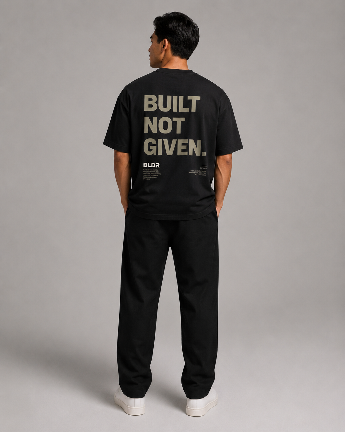 Person wearing a black t-shirt with 'BUILT NOT GIVEN' text on the back against a gray background