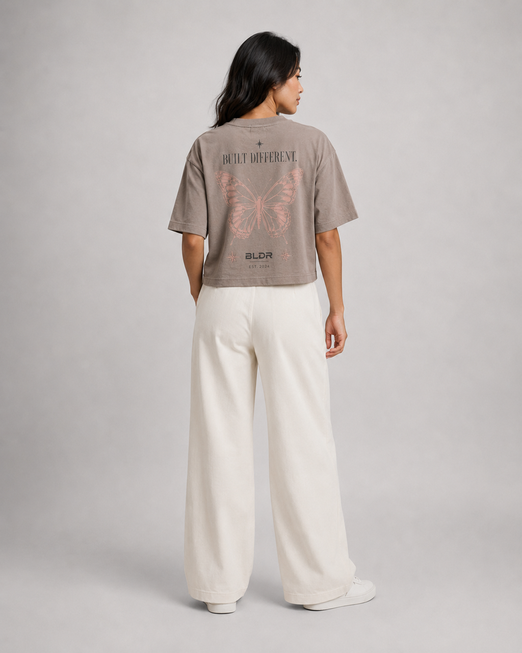 Person wearing a beige t-shirt with text and graphics on the back, standing against a plain background