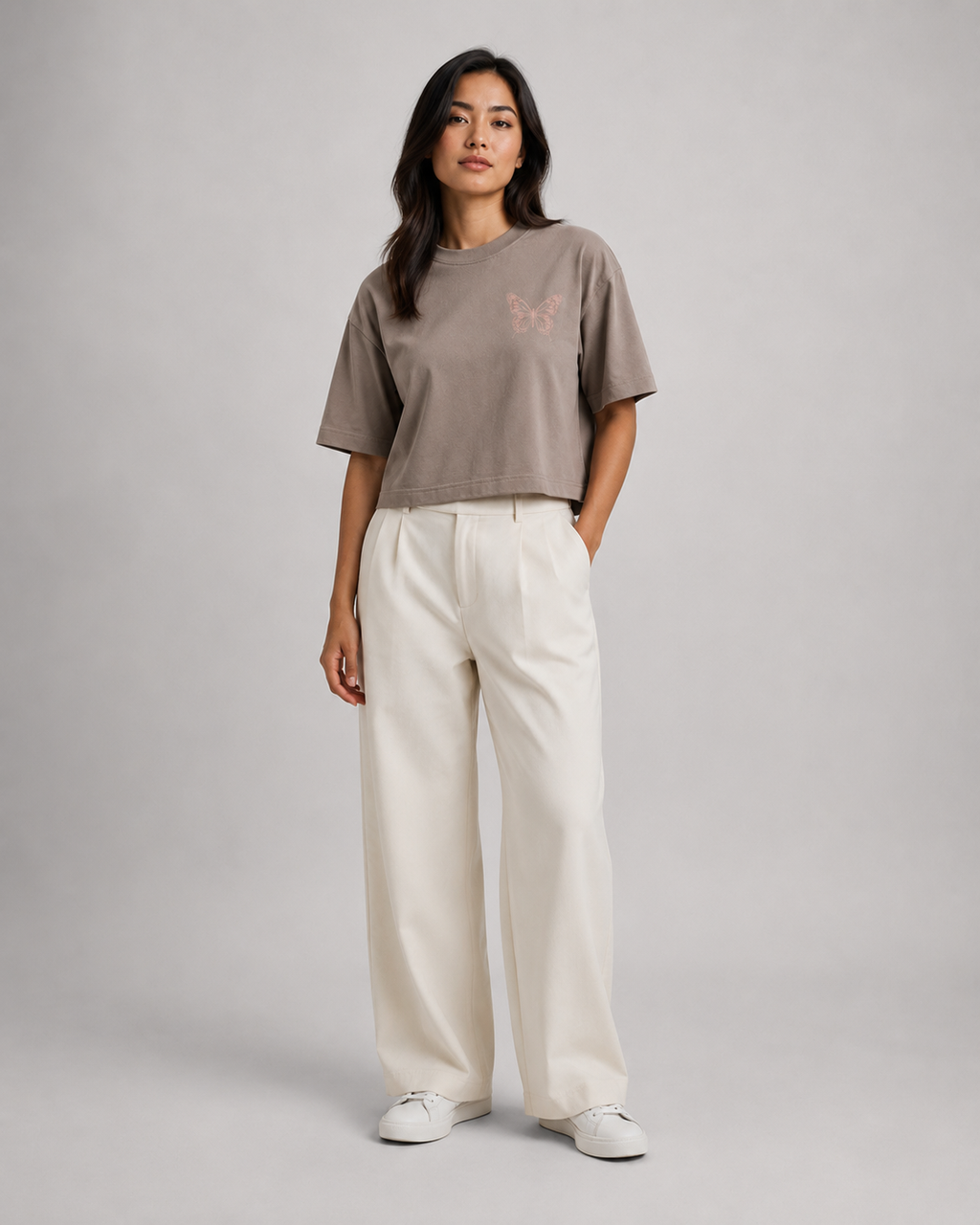 Woman wearing a brown t-shirt and white pants on a gray background