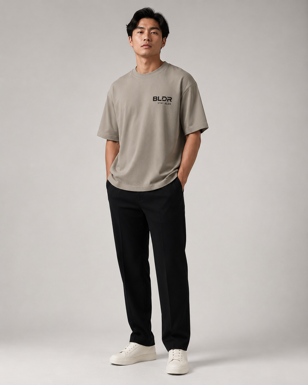 Man wearing a beige t-shirt with a logo, black pants, and white shoes on a gray background