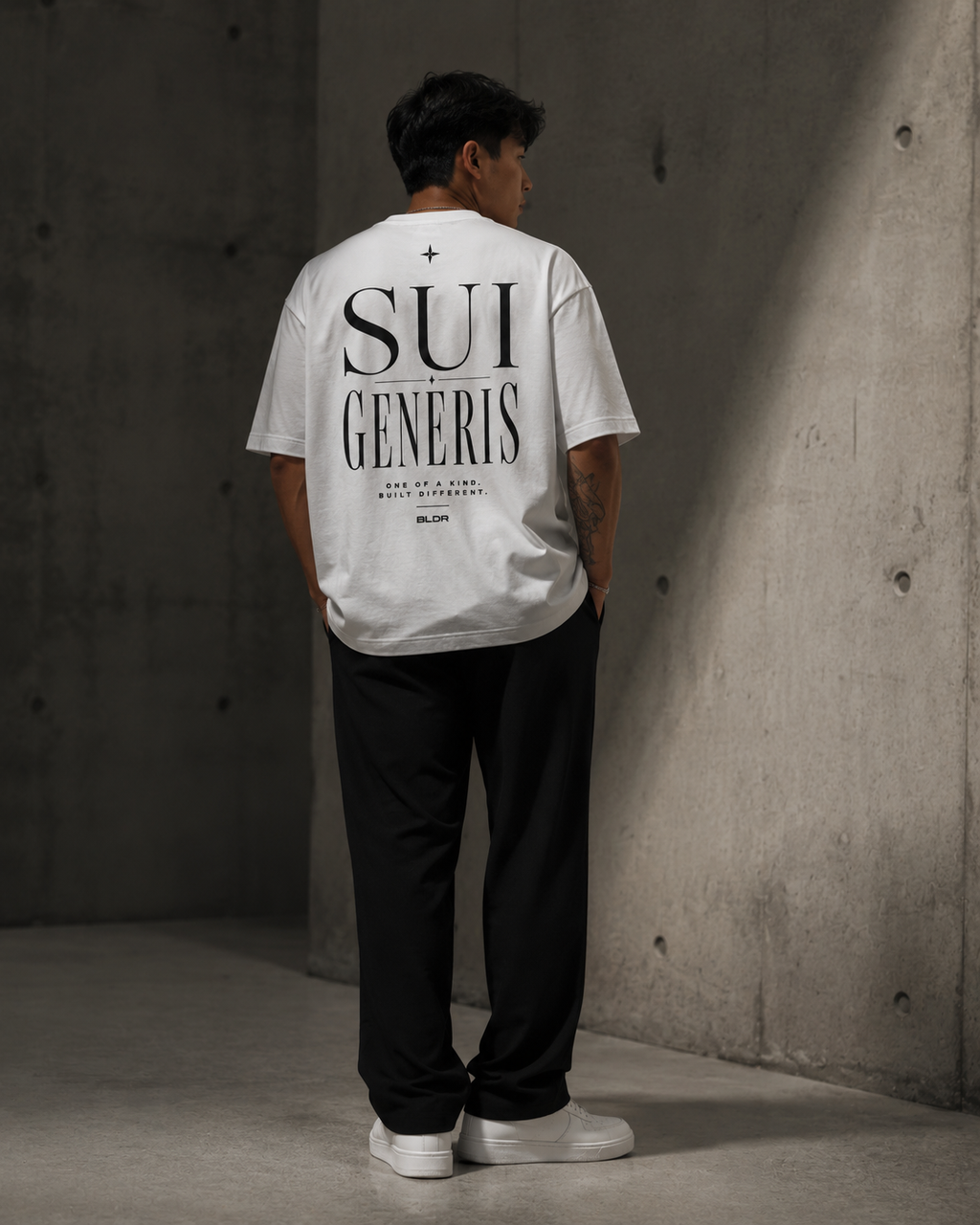 Person wearing a white t-shirt with 'SUI GENERIS' text, standing against a concrete wall.