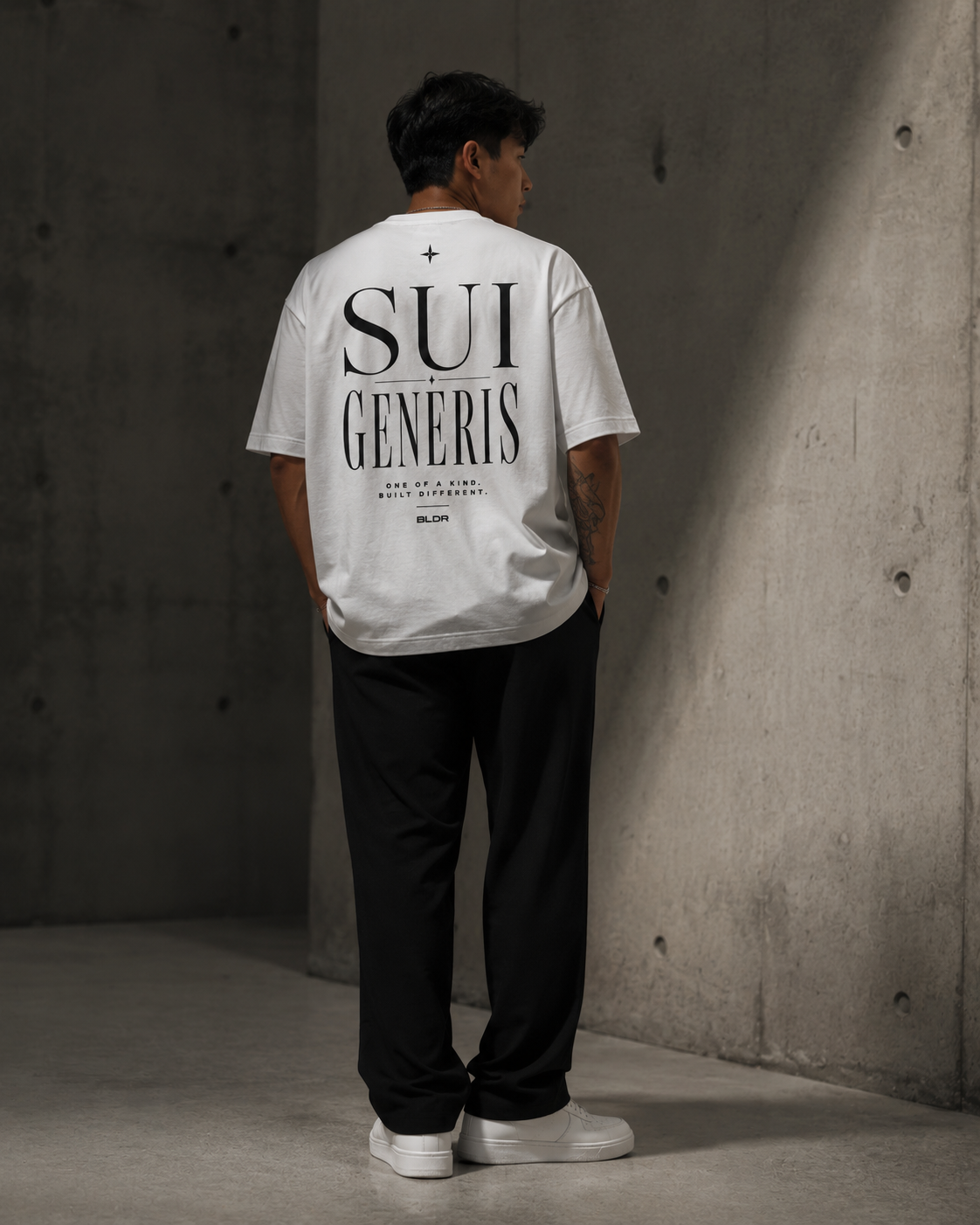 Person wearing a white t-shirt with 'SUI GENERIS' text, standing against a concrete wall.